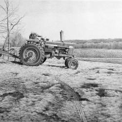 A graphite drawing of an Iowa farmer on a tractor getting ready to do spring planting.